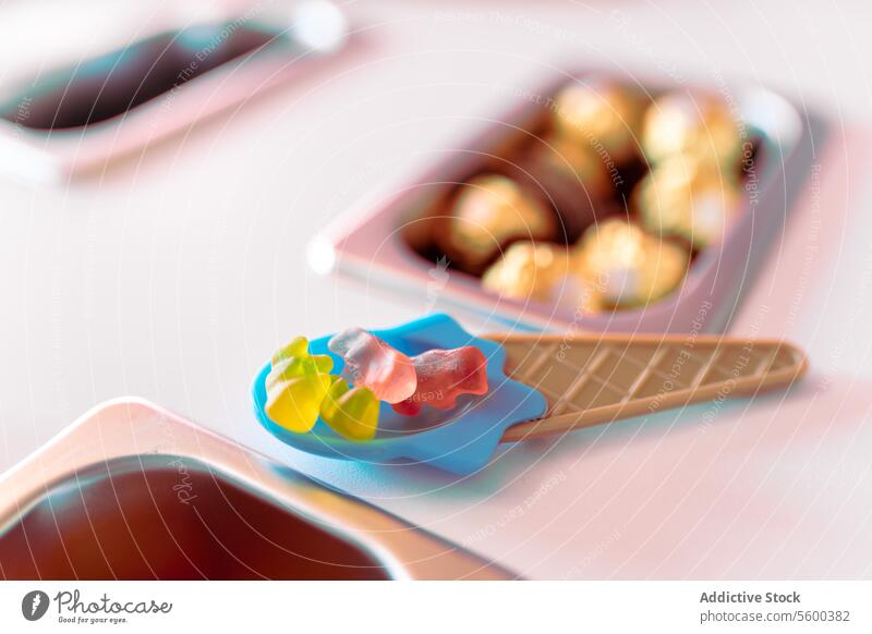 Close up photo of an ice-cream shaped spoon filled with teddy bear gummies on a counter topping gummy tray metal rolled ice cream colorful preparation shop