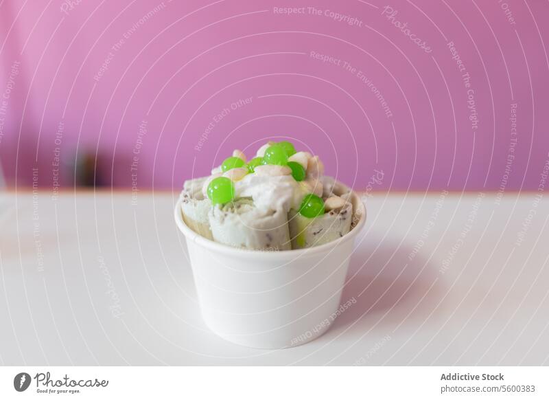 Close up of a rolled ice cream decorated with green bubbles and yogurt toppings spoon molecule tub milk work white preparation shop parlor close up tasty