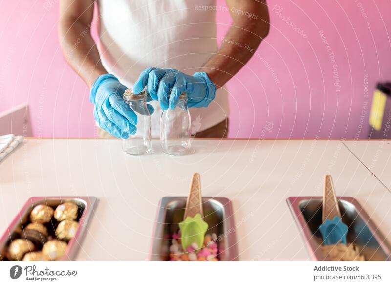 An ice-cream parlor worker is preparing two empty jars to prepare rolls on a counter next to topping trays man adult mature hispanic latin white shirt milk