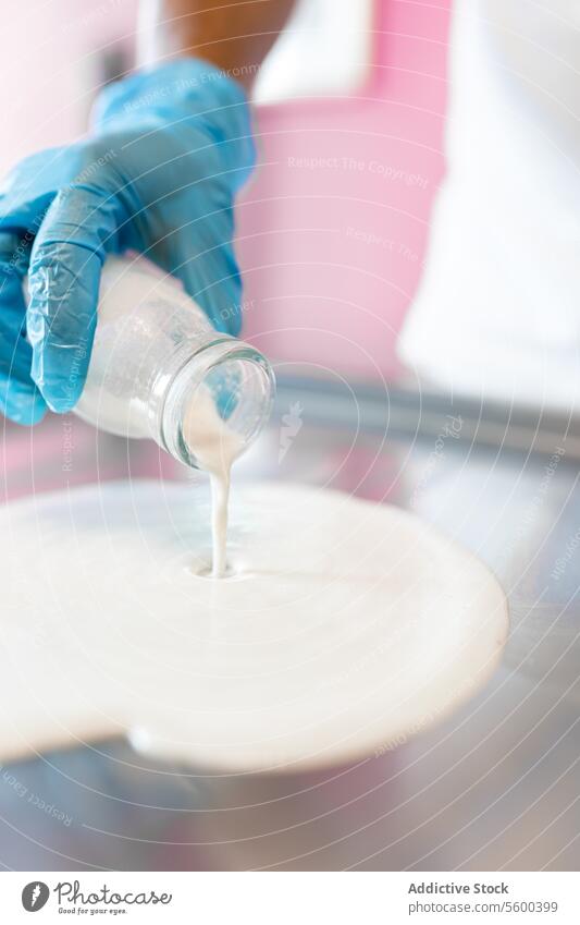 A worker is dropping milk with a jar on a rolled ice cream machine liquid tray counter topping white preparation shop parlor handmade production freeze steel
