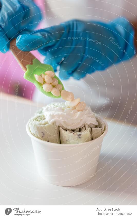 A worker is decorating a rolled ice cream tub with yogurt bubble toppings with a spoon man adult decorate molecule milk chocolate nut crunchy almond white