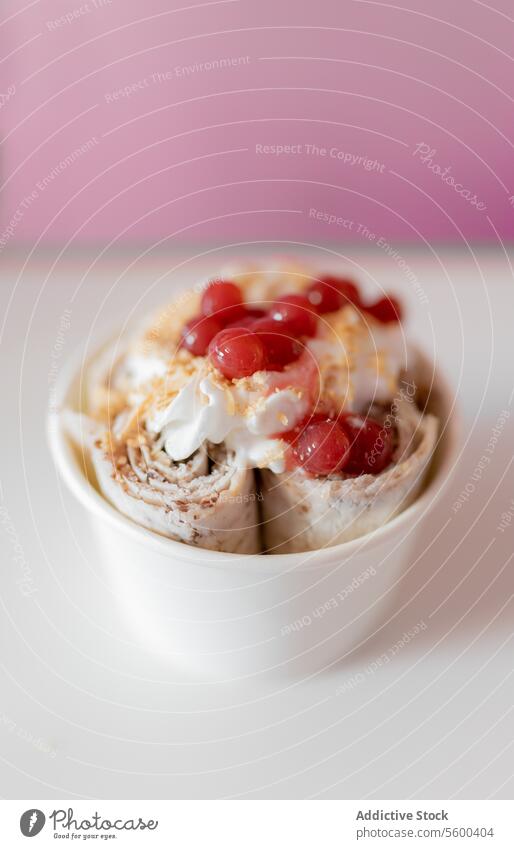 Close up of a rolled ice cream decorated with strawberry bubbles and nut toppings spoon molecule tub milk work chocolate crunchy almond white preparation shop