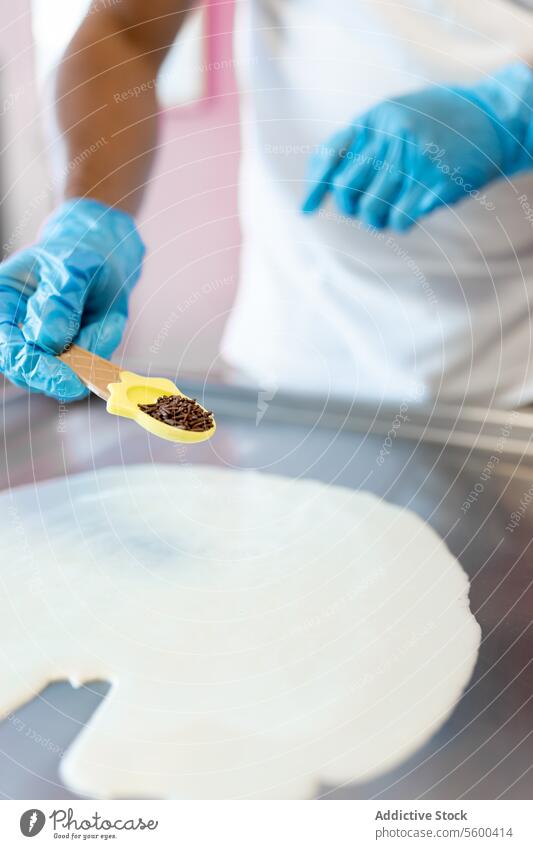 A worker is preparing a rolled ice cream with milk and chocolate chips on the freeze machine jar spoon mix drop liquid tray counter topping white preparation