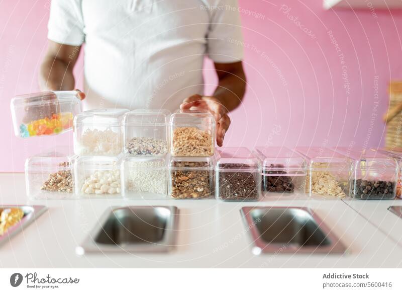 An ice-cream parlor worker is preparing all the toppings for the day on the counter man adult mature hispanic latin white shirt tray milk metal rolled chocolate