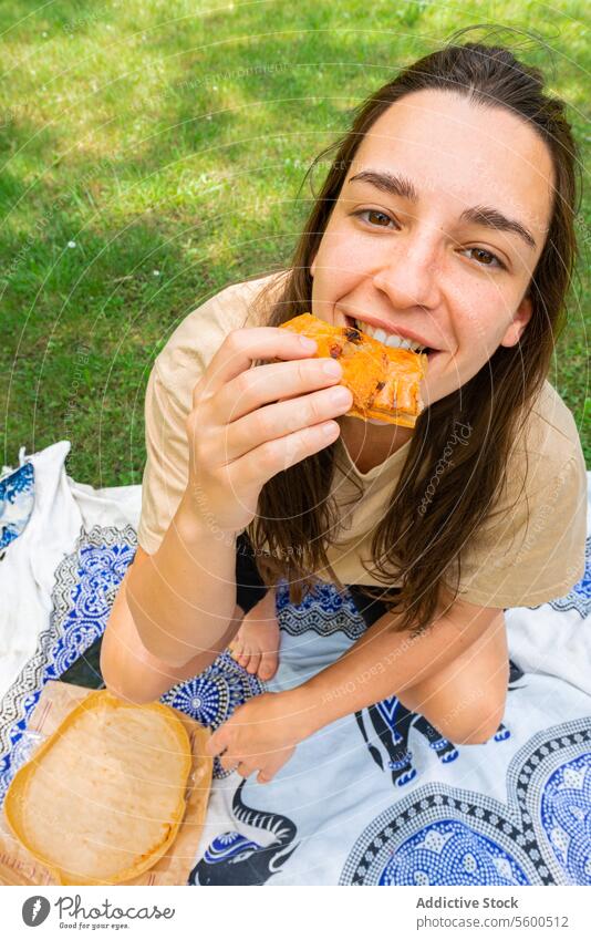 Young woman enjoying a picnic sandwich in the park eating happiness relaxation blanket sunny outdoors cheerful enjoyment snack leisure summer grass nature lunch