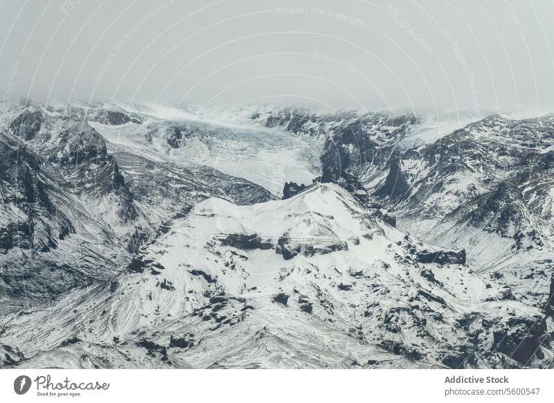 Aerial view of Snowy Mountain Expanse under Gray Sky snowy rugged landscape mountain ridges gloomy sky nature winter cold outdoor wilderness white altitude