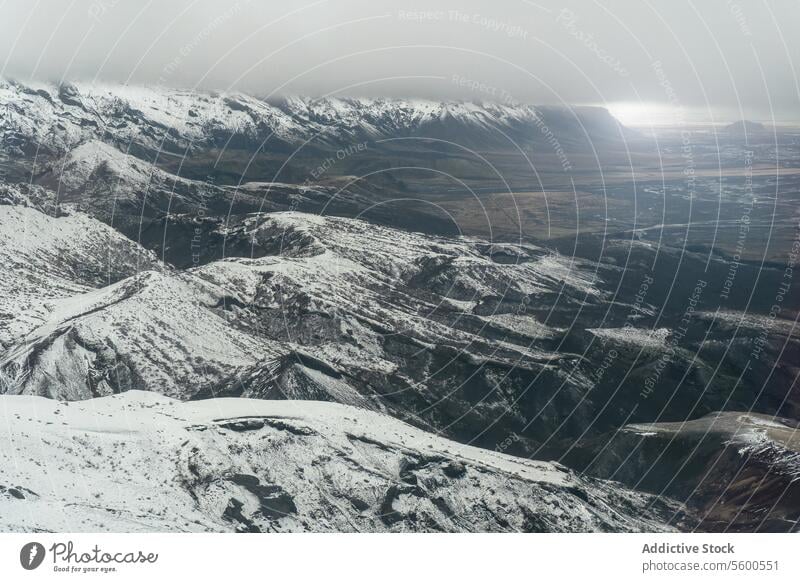Aerial view of snowy mountainside with valley dramatic sunlight clouded horizon landscape nature winter cold outdoor vast wilderness white altitude highland