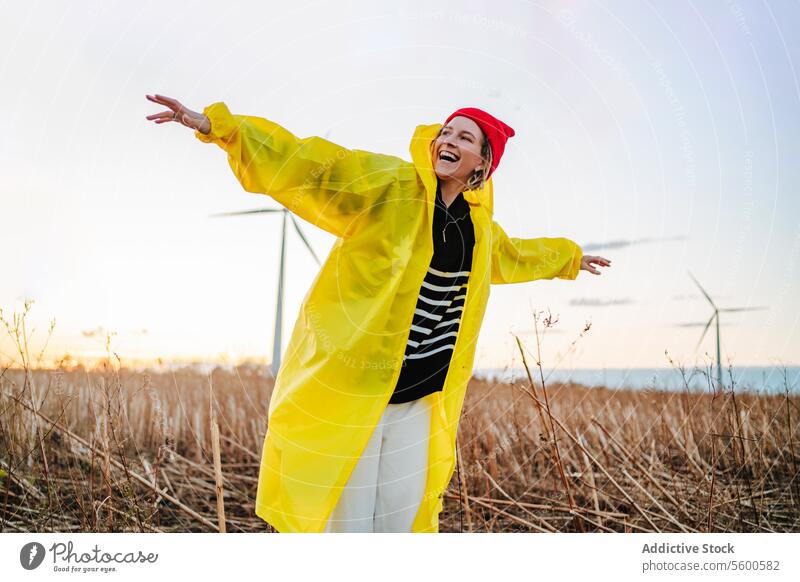 Energetic Person Enjoying a Sunset Near Windmills person happiness freedom sunset windmill field yellow raincoat energetic outdoor nature turbine renewable