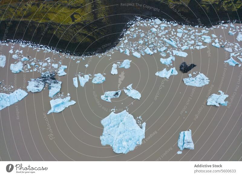 Aerial view of glacial ice on river aerial brown white float Vatnajökull national park Iceland terrain rugged contrast shoreline piece chunk melting environment
