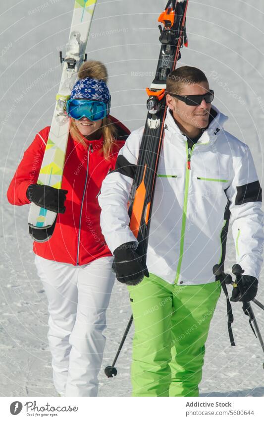 Couple walking with ski equipment in Swiss Alps couple alps swiss winter sport snow sunny ski attire colorful activity mountain outdoor vacation leisure travel