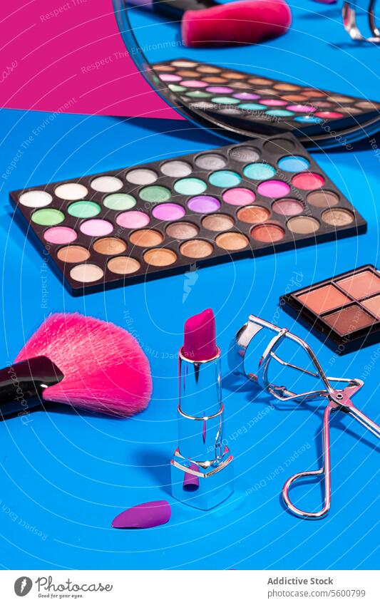 Makeup essentials on blue and pink background makeup beauty eyeshadow palette lipstick eyelash curler blush brush sponge compact powder surface backdrop