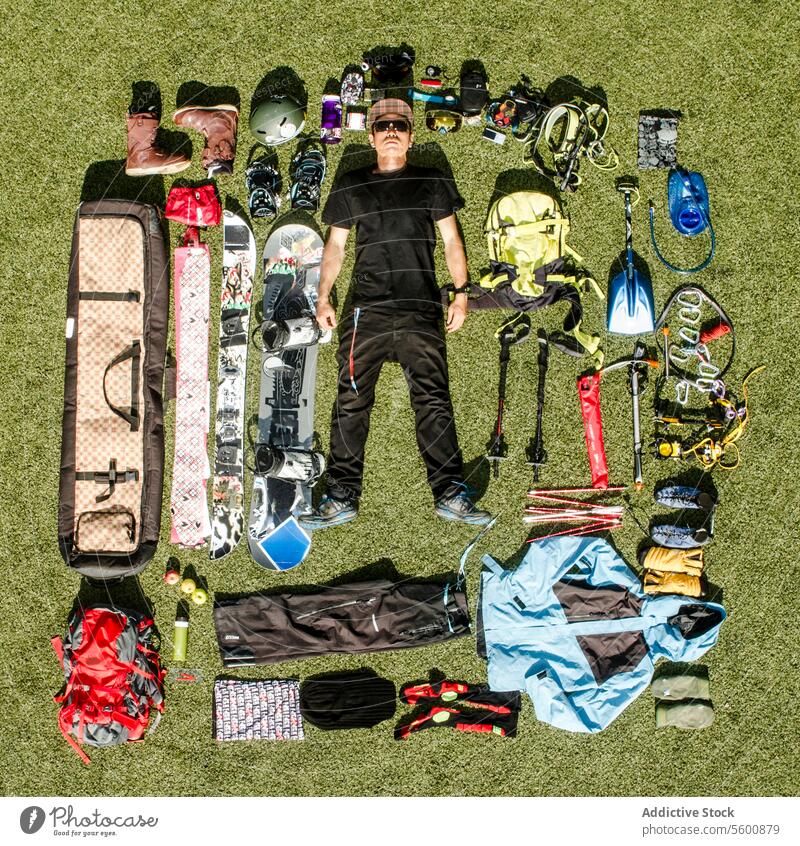 Top view of serious man in black clothes and sunglasses with various hiking equipment lying on meadow young hiker casual attire grass land tool full body