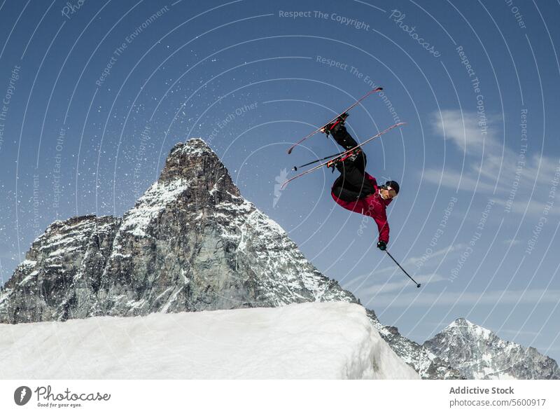 Anonymous carefree man skiing and jumping on snowy mountain while enjoying winter day at Swiss Alps skier active pole vacation adventure motion mid-air sky