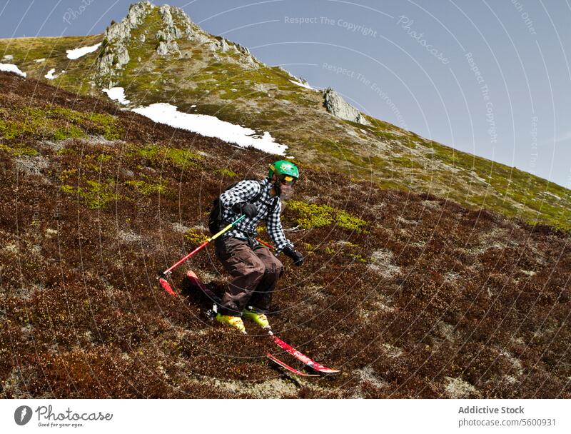 Side view of young man in casual clothes skiing on grassy land during vacation at Swiss Alps hiker hill full body carefree hiking skier pole casual attire