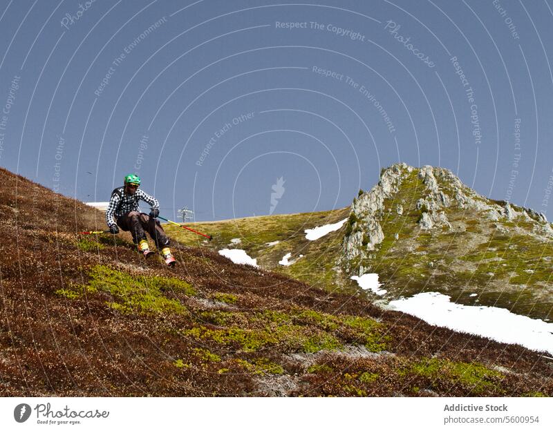 Young man in casual clothes skiing on grassy land during vacation at Swiss Alps hiker hill full body carefree hiking skier pole casual attire helmet beautiful