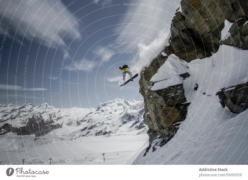 Anonymous snowboarder jumping from mountain in winter day against cloudy sky at Swiss Alps person rock snowboarding swiss alps vacation unrecognizable scenic