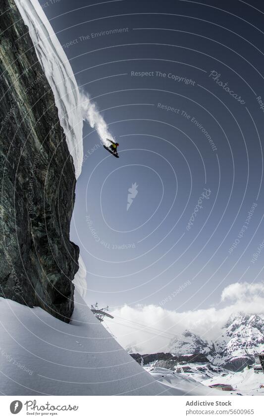 Side view of anonymous snowboarder jumping from mountain in vacation against clear sky at Swiss Alps enjoy distant adventure mid-air blue sky from below nature