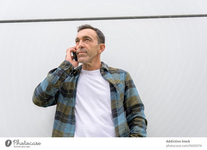 Thoughtful man talking on smartphone male gadget device mobile casual conversation style using modern checkered shirt speak call street cellphone beard