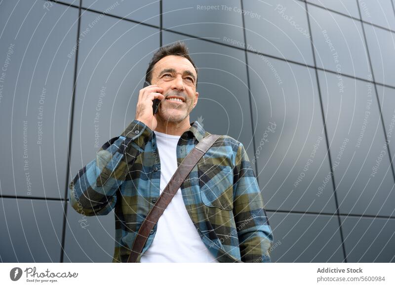 Cheerful young man talking on smartphone male casual hipster beard street style wall modern conversation phone call gadget smile speak communicate cheerful