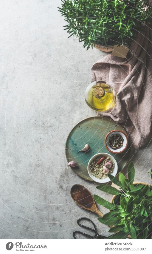 Kitchen background with various flavor ingredients and seasoning on grey concrete kitchen table: fresh herbs, oil, garlic, sage, kitchen utensils and table cloth. Food frame. Top view with copy space.