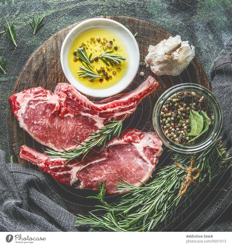 Raw meat chop on wooden cutting board with rosemary, herbs, spices and cooking oil. Top view raw top view bone cutlet butcher rib veal bbq ingredient food lamb