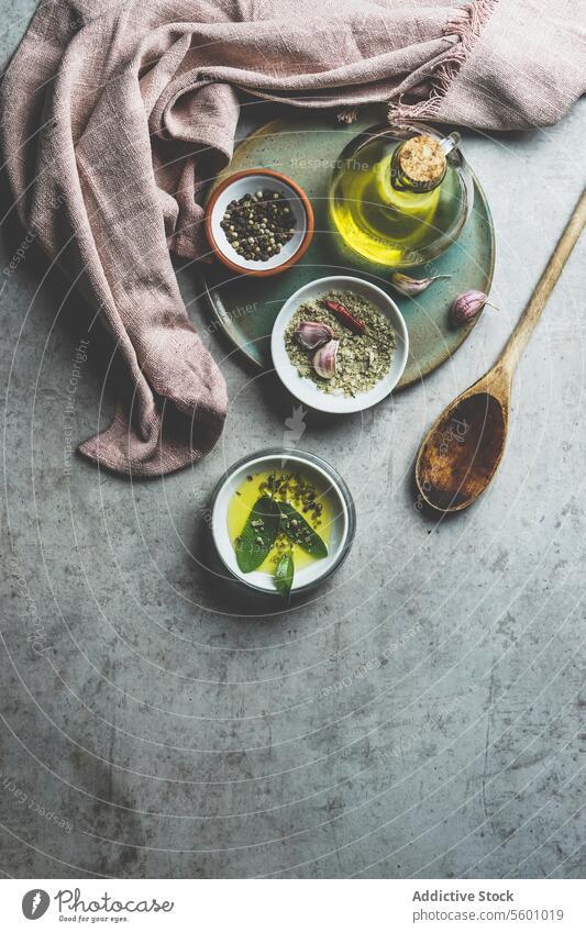 Healthy cooking ingredients on grey concrete kitchen table: olive oil, sage, garlic, pepper, salt, wooden cooking spoon, dish cloth. Cooking flavorful food at home. Top view.