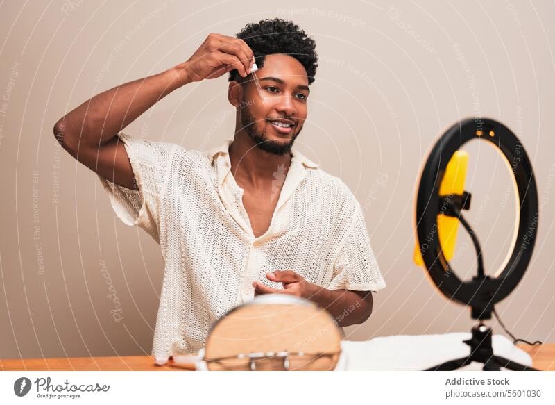 Latin man applying skin product at home with mirror and light latin grooming ring light hair care smile hairstyle curls wooden table skin care routine beauty