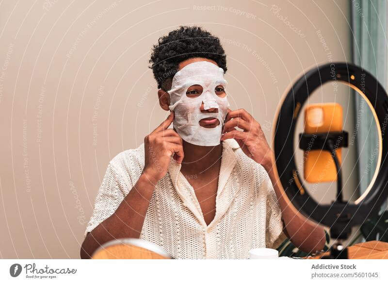 Young latin man applying a facial skincare mask while looking in the mirror. facial mask beauty self-care pampering routine grooming wellness health cosmetic