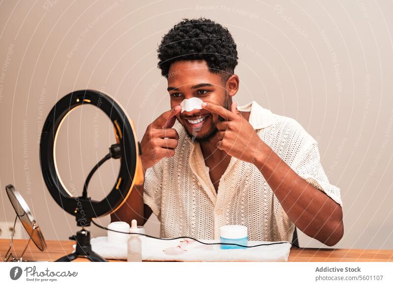 latin man applying skincare routine with smile nose strip self-care ring light smiling young facial treatment happy cheerful grooming wellness health beauty