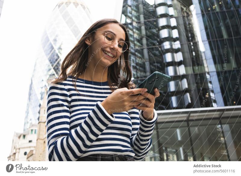 Smiling Woman Using Smartphone in London Cityscape woman smartphone london city urban skyline happy striped top engagement building modern technology