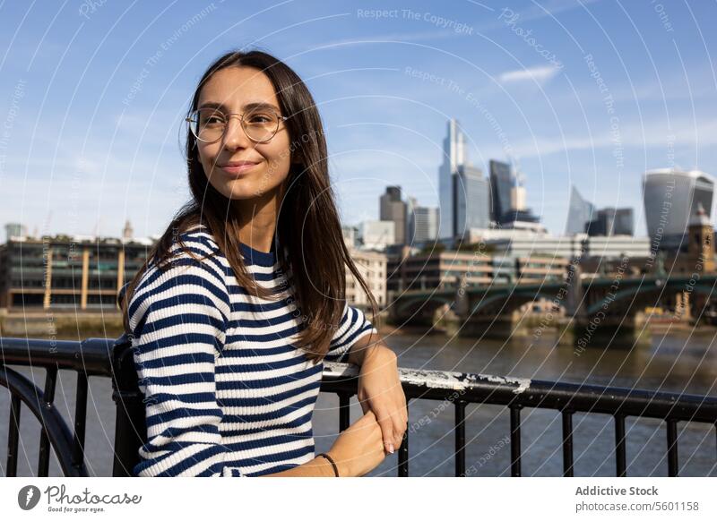 Young woman enjoying the cityscape by the Thames london thames glasses smile striped shirt river background young adult female leisure travel tourism outdoor