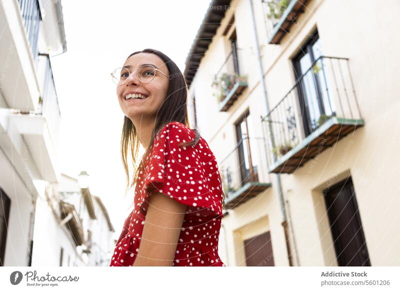 Low angle of happy woman in eyeglasses looking away against old buildings in town tourist smile cheerful casual attire standing beautiful vacation lifestyle