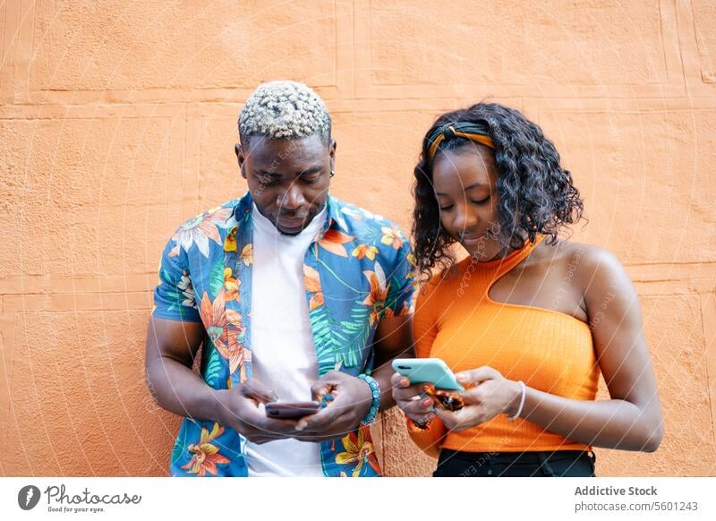Young black friends using smartphone in the street young couple smiling happy lifestyle outdoor mobile technology urban casual man woman cellphone portrait