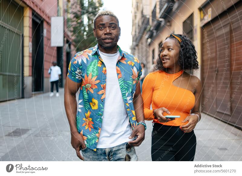Young black friends walking in the street young couple smiling smartphone happy lifestyle outdoor mobile technology urban casual man woman cellphone portrait