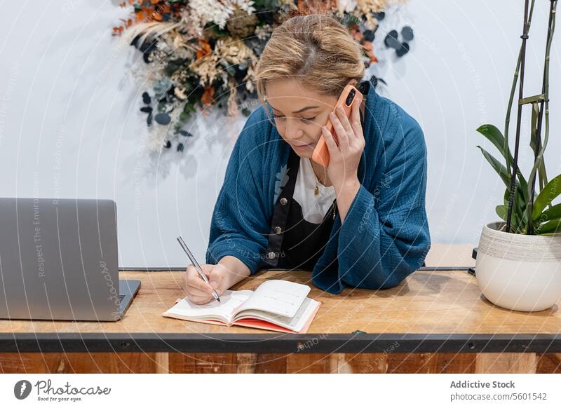 Businesswoman organizing her schedule with notes and laptop and speaking on smartphone businesswoman writing planner desk wooden organized focused management