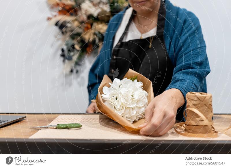 Anonymous person crafting a bouquet with white flowers and paper wrap table wooden twine scissors floral arrangement hobby design decoration work nature plant