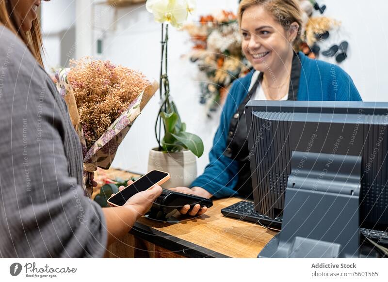 Customer making a contactless payment at a flower shop woman customer smartphone NFC technology florist cashier assisting checkout retail purchase business