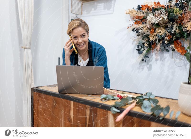 Florist taking order over phone with laptop at counter woman florist mobile phone smiling business work technology businesswoman communication flowers workshop