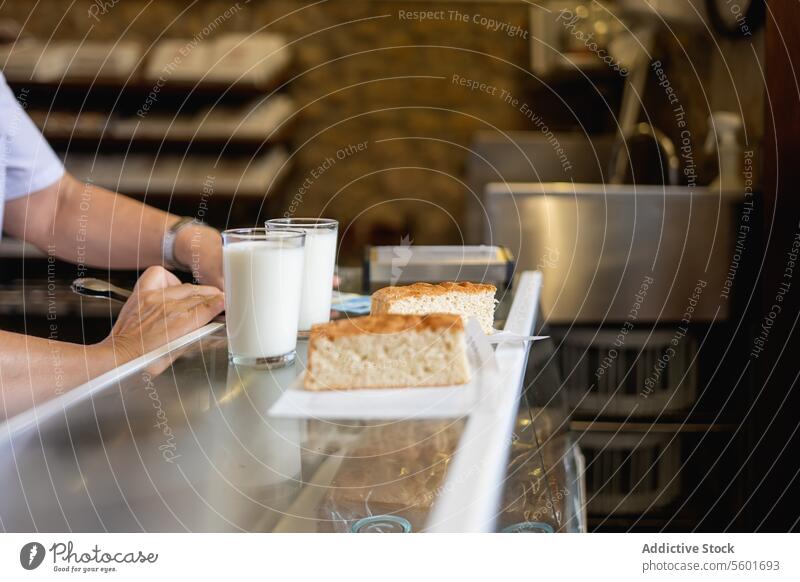 Unrecognizable person putting two glasses of milk and cake on the counter Milk bakery arm food dairy drink bread breakfast snack cafe kitchen faceless anonymous