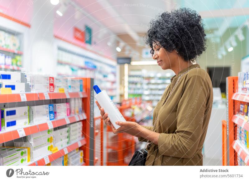 Black female holding bottle in pharmacy store woman hand check information prescribed product label drugstore blurred background closeup ingredient health care