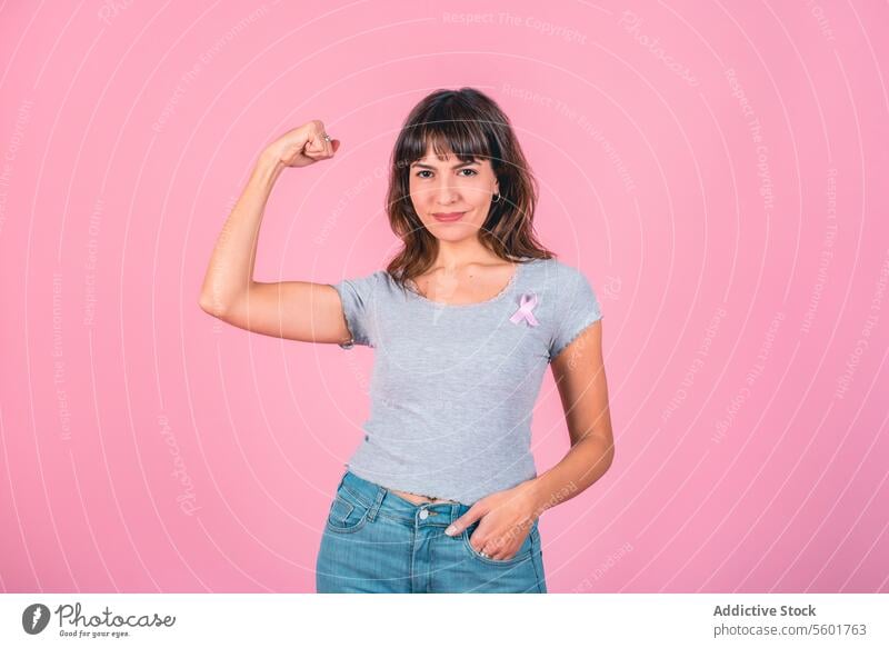 A woman wearing pink breast cancer awareness ribbon while showing arm muscle. Victory over breast cancer. Breast Cancer Awareness Breast Cancer Month
