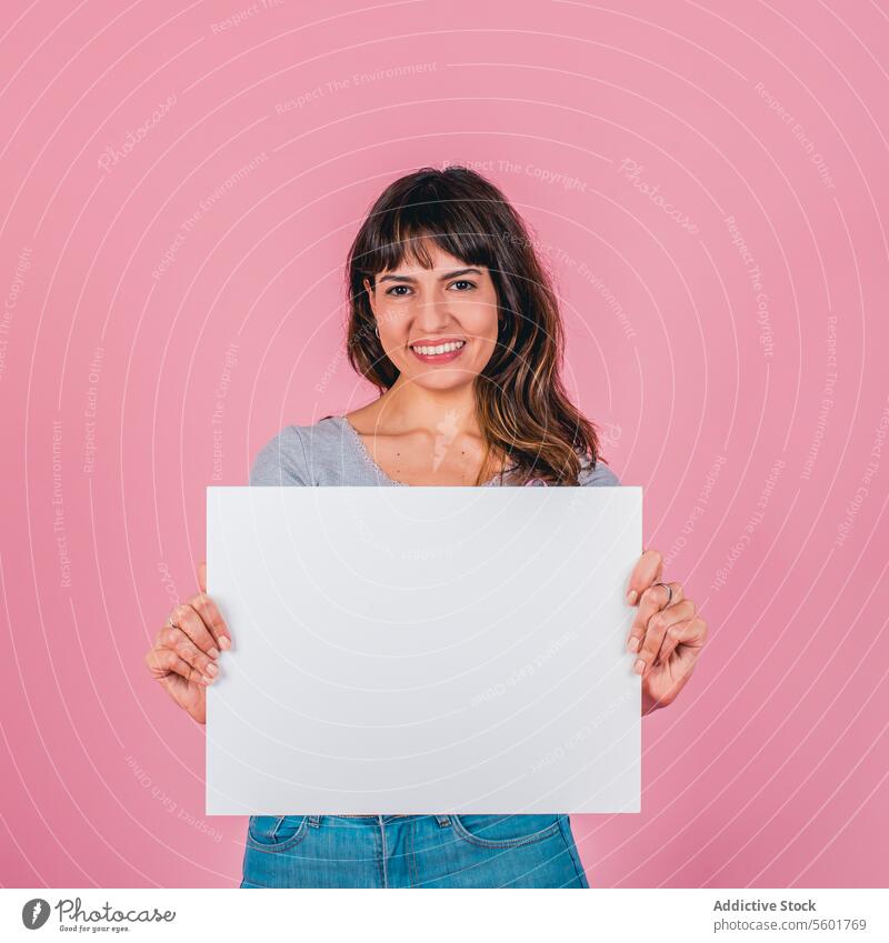 Smiling woman holding a blank sign against a pink background adult attractive beautiful beauty brown hair businesswoman copy space empty ethnicity female