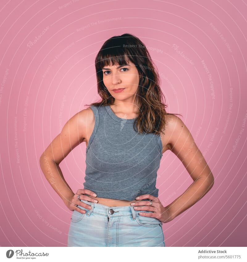 Studio portrait of a confidence woman with hands on hips while looking at camera over a pink background achievement action active adult alone attractive