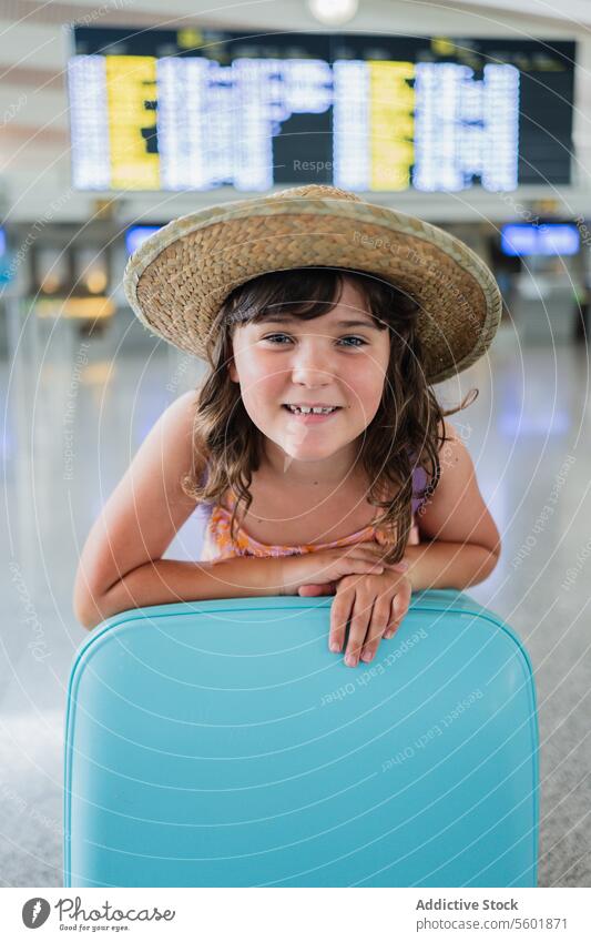 Happy girl in straw hat with blue suitcase at airport while waiting for departure at airport terminal portrait vacation holiday luggage smiling missing tooth