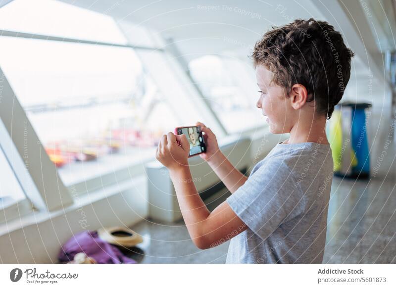 Cute boy on video call through smartphone mobile cute airport side view contemporary connection travel vacation holiday holding smiling standing device internet
