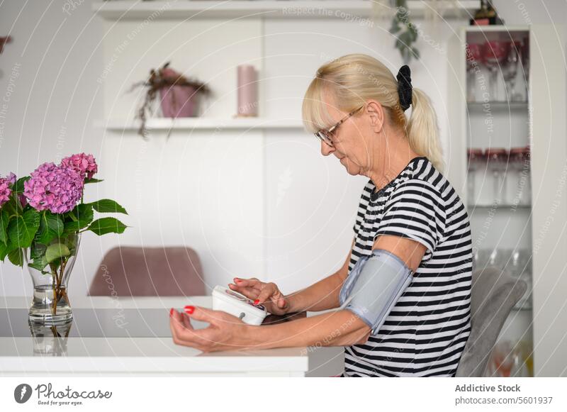 Senior woman measuring blood pressure at home check senior measure routine table patient focus examine mature attentive sit female daily concentrate lifestyle