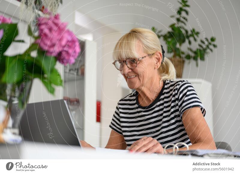 Happy mature woman using laptop in living room at home freelance remote work project positive browsing device gadget online distance internet indoors senior