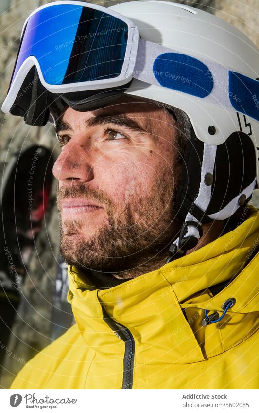 Confident skier with helmet and goggles looking aside man beard yellow jacket close-up thoughtful distance expression outdoor winter sport snow mountain
