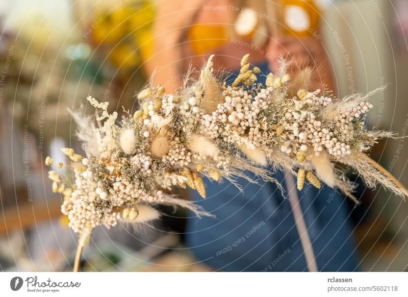 Close-up of a dried flower wreath held by a person in a blue apron, blurred background close-up person holding floral dried flowers handmade floristry natural