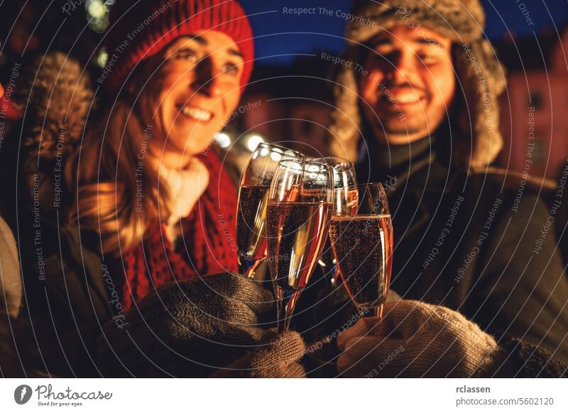 Couple toasting with champagne glasses in winter evening at a christmas market group friends new year couple celebration happy joy outdoor cold warm clothing